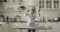 Cheerful mature baker woman dancing and singing at kitchen table