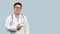 Cheerful middle aged korean male doctor in white coat and glasses point finger on copy space