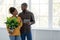 Cheerful millennial african american man and woman look at each other hold tablet and plant on window background