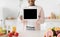 Cheerful millennial black female shows tablet with empty screen at kitchen interior near table with organic fruits