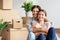 Cheerful millennial caucasian guy hugging woman sit among boxes, plants, rest from packing belongings