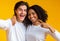 Cheerful millennial couple taking selfie, posing together over yellow background