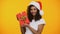 Cheerful mixed-race woman in santa claus hat holding red giftbox and smiling
