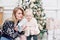 Cheerful mom and her cute daughter baby open a gift. Parent and little child having fun near Christmas tree indoors