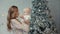 Cheerful mother kissing cute child near christmas tree in modern apartment.