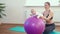 Cheerful mother playing with infant, making baby fitness exercises on big ball