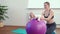 Cheerful mother playing with infant, making baby fitness exercises on big ball