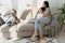 Cheerful mother sitting on couch in cozy light living room holds on lap tickles of little son enjoy funny activities on weekend at