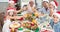 Cheerful multi-generational family in santa hats toasting drinks at dining table