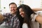 Cheerful multiethnic couple in love sits in embrace in cozy living room at home