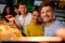 Cheerful multiracial friends taking selfie in pizzeria.