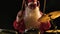 Cheerful musician dressed as Santa Claus plays drums on a black studio background. A man in a red festive suit with a