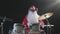 Cheerful musician dressed as Santa Claus plays drums on a black studio backlit background. A man in a red festive suit