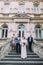 Cheerful newlywed pair with happy groomsman and bridesmaid posing at the stairs of classical building