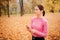 Cheerful and nice young woman stands alone in park. Jogger listen to music through headphones. She holds phone in hands