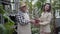 Cheerful old Caucasian gardener giving pot with cactus to positive brunette young woman. Happy brunette lady buying