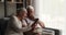 Cheerful older spouses rest on sofa with modern cellphone