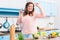 cheerful overweight woman listening music in headphones and dancing at table with fresh vegetables in kitchen