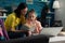 Cheerful parent sitting beside daughter holding school book reading together