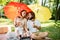 Cheerful parents with two kids have a rest on the lawn under the bright red and yellow umbrellas covering them from the