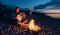 Cheerful percussionist girl playing djembe sitting on beach by the fire at sunset