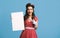 Cheerful pinup lady in retro outfit holding blank advertising board with copy space on blue background, mockup