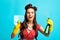 Cheerful pinup lady in retro style wear doing cleanup with rag and spray detergent on blue studio background