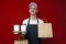 Cheerful pizza delivery man in uniform on a red background gives a ready order, a happy courier guy holds coffee and bag and