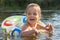 Cheerful playful littl girl swimming with help of swimming circle, opening her mouth widely with excitement, looking aside,