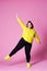 Cheerful plus size model in casual clothes, fat woman in black jeans and yellow jumper on pink background