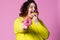 Cheerful plus size model eating doughnuts, fat woman overeats on pink background