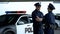 Cheerful policeman and policewoman communicating on parking lot, patrolling