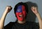 Cheerful portrait of a man with the flag of Chinese Taipei or Taiwan painted on his face on grey background.