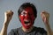 Cheerful portrait of a man with the flag of the Hong kong painted on his face on grey background.