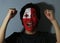 Cheerful portrait of a man with the flag of Tonga painted on his face on grey background.