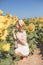 Cheerful positive young woman posing on camera among field of sunflowers. Happy girl  in straw hat during summertime. Harvest