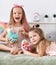 Cheerful pretty small girls sisters kids with long hair relaxing on bed and playing with toys dolls together