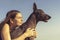 Cheerful pretty young girl sitting and hugging her dog xoloitzcuintli at the blue sky at sunset