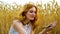 Cheerful redhead girl playing with wheat ear in field in summer