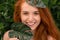 Cheerful redhead woman laughing through monstera leaves