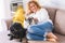 Cheerful relaxed adult pretty woman at home lay down on the sofa with her two best friends dogs pug - concept of people and