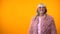 Cheerful retiree lady in funny pink coat and round sunglasses posing on camera