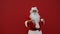 Cheerful santa dancing on a red background with a plate of chocolate chip cookies and a glass of milk in his hands. Christmas