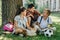 Cheerful schoolkids talking while sitting on lawn under tree