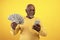 Cheerful senior black man with money and cellphone winning lottery or casino bet on orange studio background