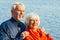 Cheerful senior citizens woman and man are standing and hugging on the lake, against the background of the bridge