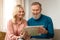 Cheerful Senior Couple Holding Paper Travel Map, Planing Vacation Indoor