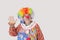 Cheerful senior male clown waving hand while looking away over gray background