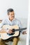 Cheerful senior man in glasses playing acoustic guitar