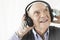 Cheerful senior man listening music through headphones against white background